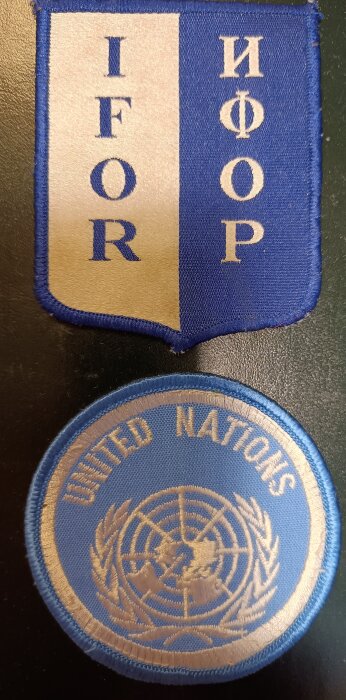 Tygmärken från FN:s IFOR-styrkor i Bosnien Hercegovina 1995, visar FN:s logotyp och texten "United Nations".