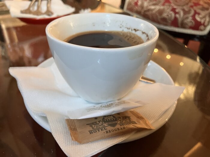 Kaffekopp på ett bord med servett och sockerförpackning märkt "Hotel Moskva Beograd" bredvid.