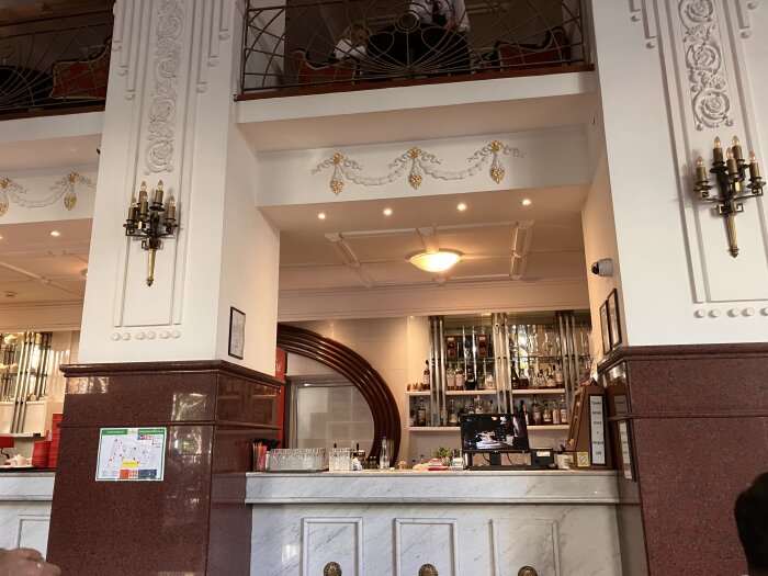 Elegant inredd restaurangbar med marmor och dekorativa detaljer, flaskor uppställda i bakgrunden och levande ljus på väggarna.