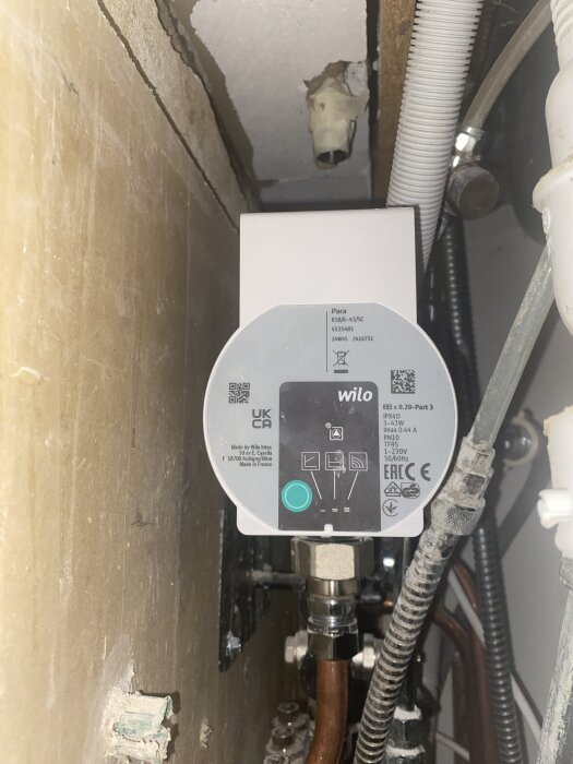 Cirkulationspump från Wilo monterad i ett trångt utrymme med kopparrör och kablar synliga. Den gröna knappen verkar inte fungera enligt användaren.