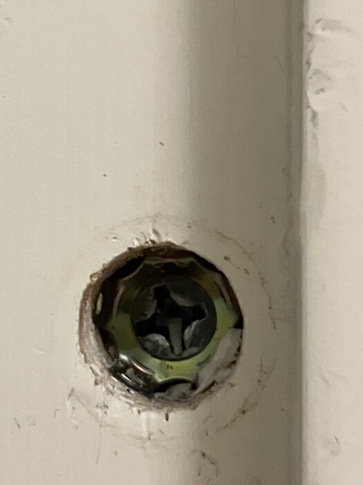 En närbild av en delvis utskjuten skruv i en dörrkarm, med synliga skador runt skruvhålet.
