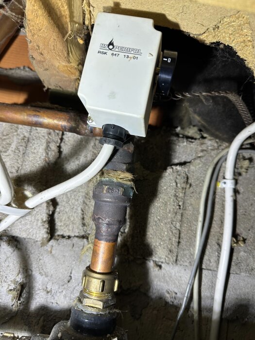 Shuntventil och rörinstallation under ett fritidshus med märkningen Höverifal RSK 647, omgiven av kablar och isolering.