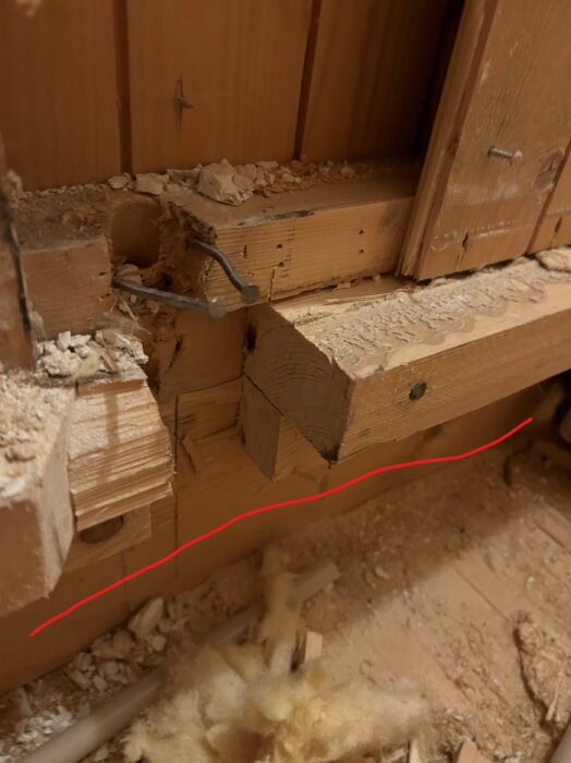 Närbild av träbjälkar med rött streck som markerar befintlig vägg. Synliga kablar och spån på golvet i badrum under renovering.