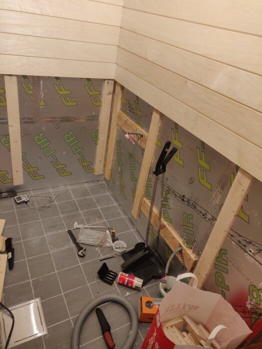 Byggprojekt i gång med träpaneler över isolering och synliga verktyg på golvet.