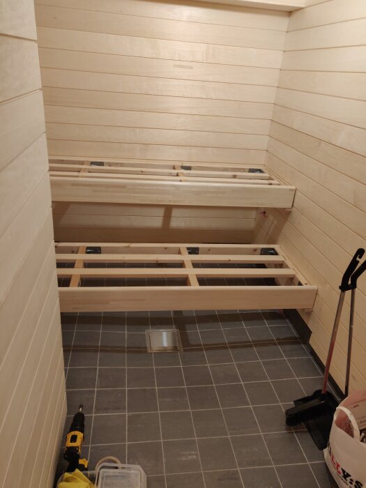 Träram och panelmontering med spikläkt syns i ett byggprojekt med golvplattor och verktyg.