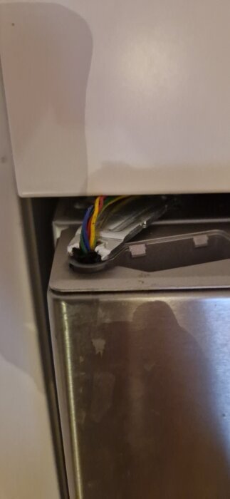 Kylskåpsdörr med synlig kabelstam, uppenbar kabelbrott, försök till reparation.