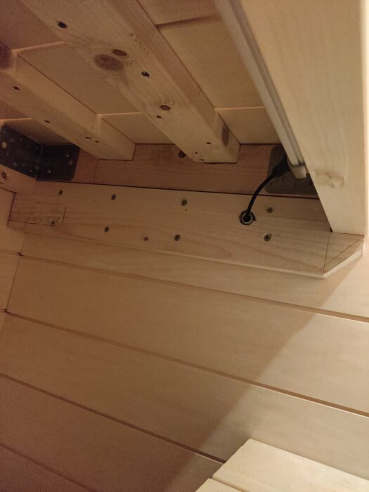 Underrede av trä med skruvar och beslag, en genomgående kabel syns.