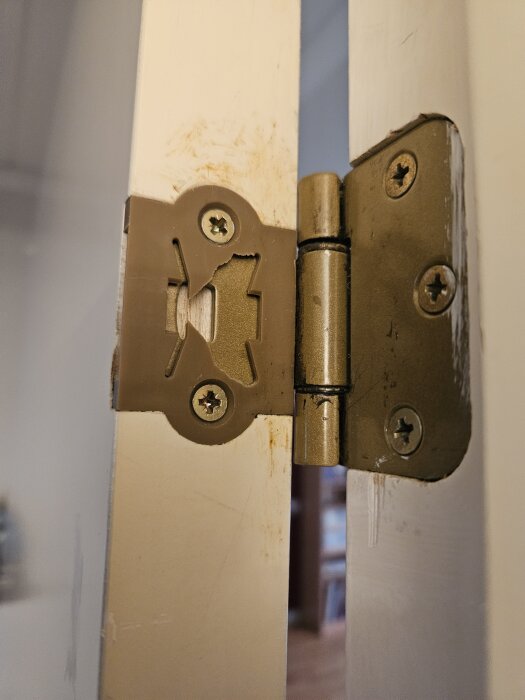 Gångjärn monterat på en vit dörr, fastskruvat med tre skruvar, av metall.