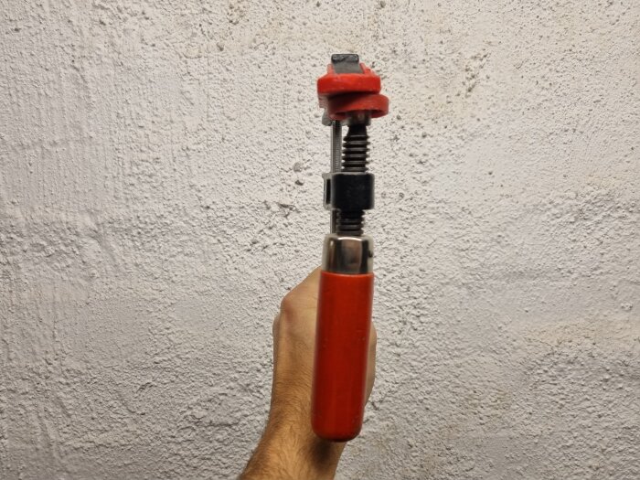 En hand håller en röd och svart tving mot en vit strukturerad vägg.