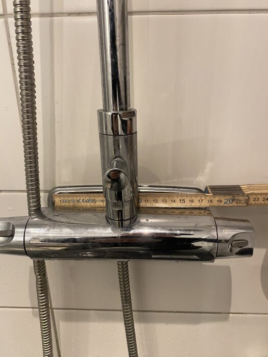 Duschtermostat med två reglage och duschslang, mätverktyg ovanpå för att mäta blandarens bredd.