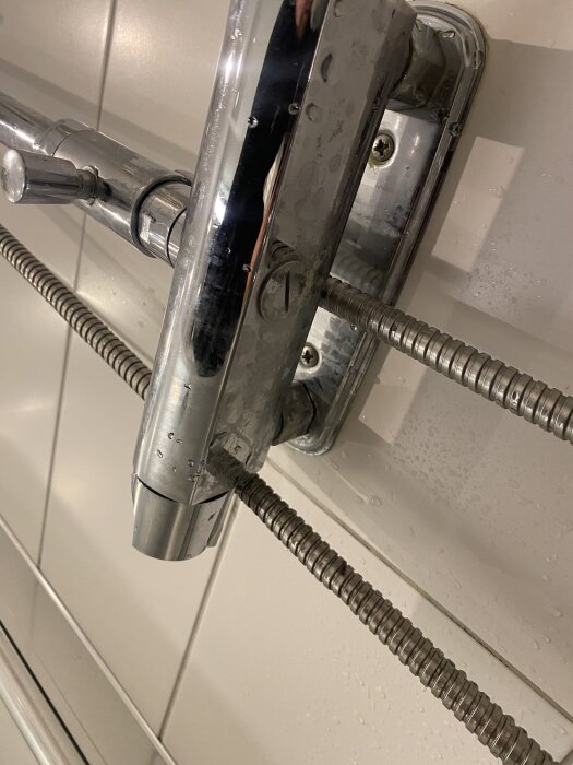 Duschblandare monterad på vit kakelvägg med två kopparrör anslutna.