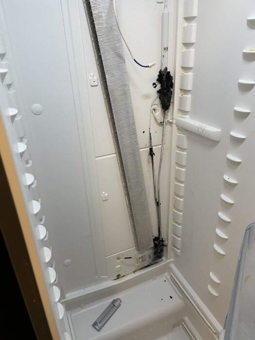 Kylskåpsinredning med borttagen kåpa, synlig svart fästmassa längs en ledning i det vita utrymmet. Eventuellt äldre och inte möglig.