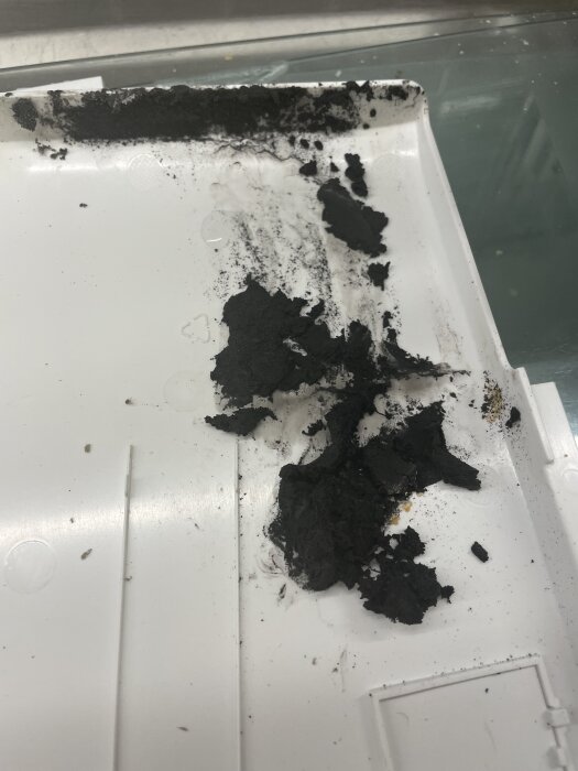 Svart fästmassa på vit yta efter borttagning av kåpor baktill vid byte av fläkt i kylskåp, ifrågasatt om det är åldrat eller ursprungligt.