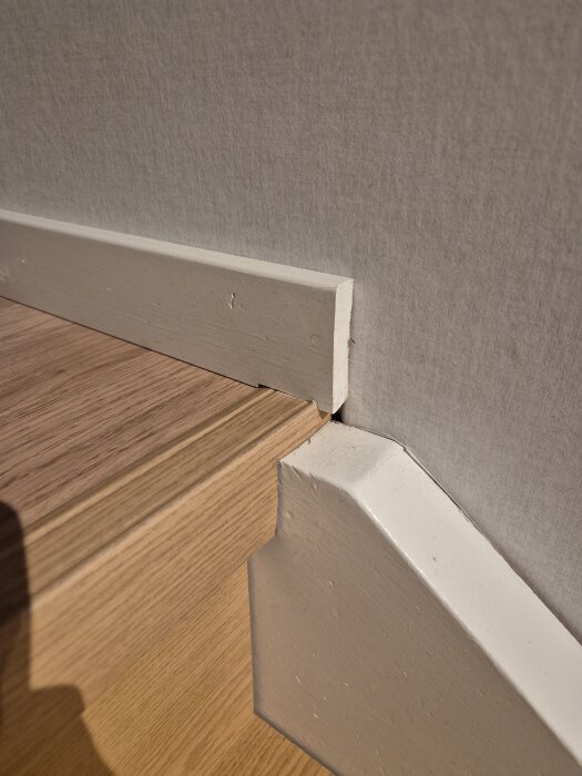 Golvlist fortsätter över trappnoslist, vitmålad ände vid trappkant.