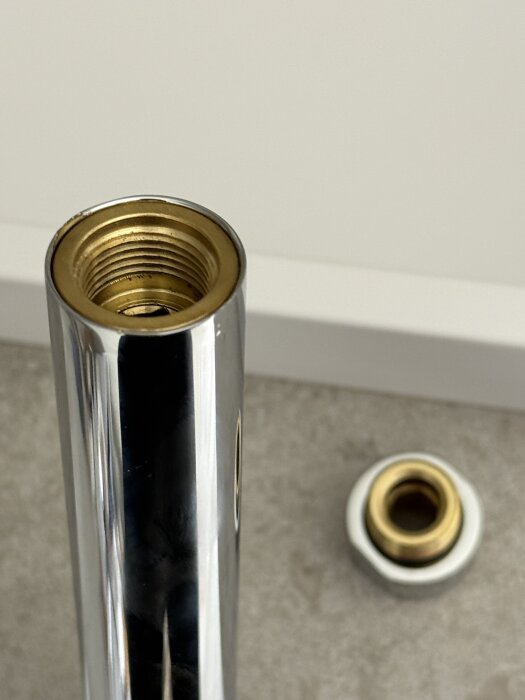 Kromad hylsa i ett duschrör, med synliga gängor inuti och en lös koppling bredvid på golvet.