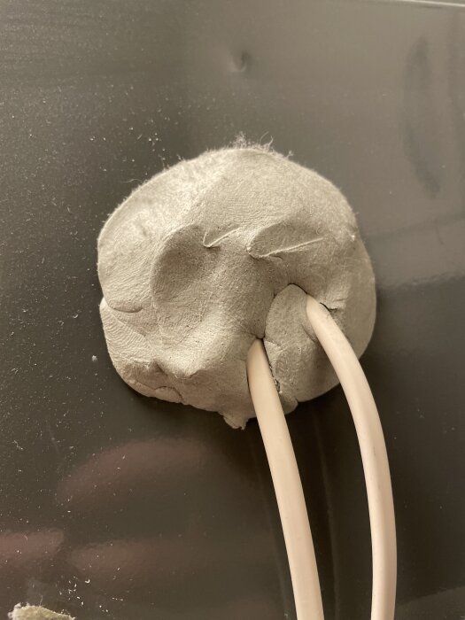 Grå massa fäst på vägg med två genomgående kablar.