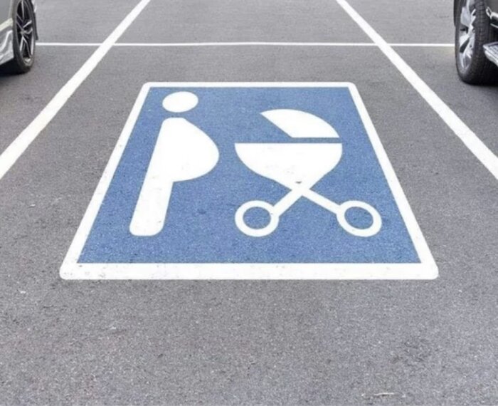 Parkeringsplats med symbol för överviktig person och grill på blå och vit skylt, omgiven av bilar.