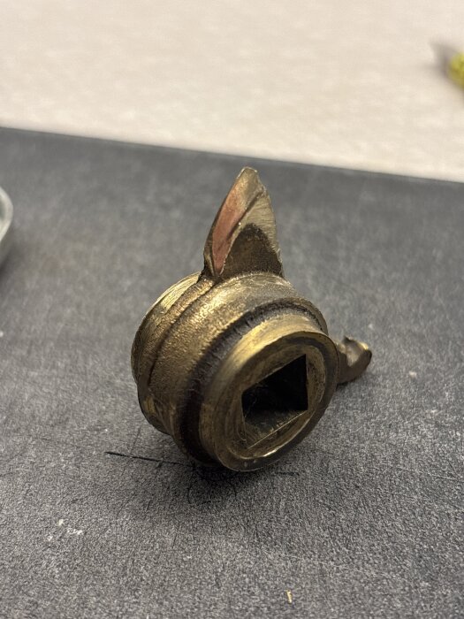 En sliten metallkomponent från en låskista visad närbild på en mörk yta.