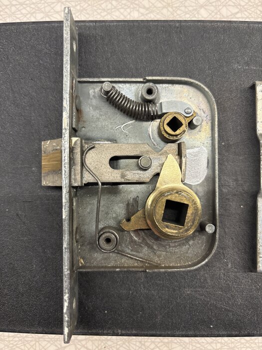 Toalettlås med synliga mekaniska delar, inklusive en fjäder och flera metallkomponenter.