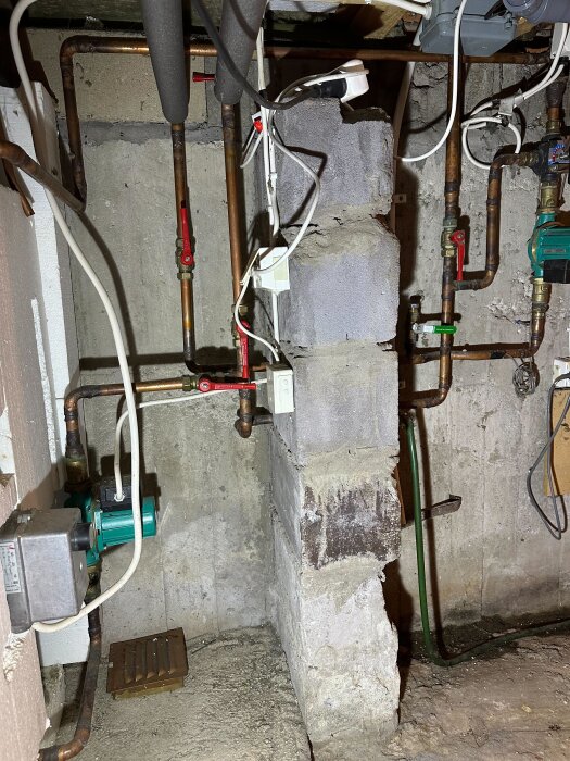 Krypgrund med rörsystem och två pumpar, pil markerar rör från vedeldad värmepanna, stenvägg och betonggolv synliga.