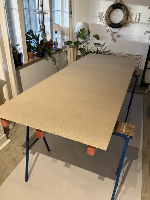 Spånskiva på bockar i grovkök omgivna av växter och lampor, del av skjutdörrsprojekt.