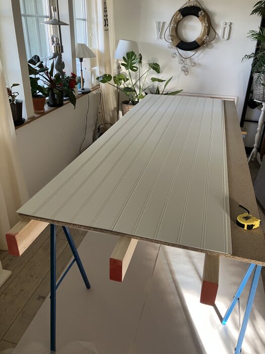 Vit pärlspontspanel på arbetsbord i ljust rum, med växter och lampor i bakgrunden, del av projekt för skjutdörrar i grovkök.