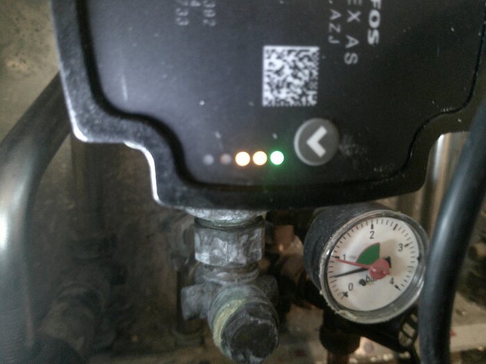 Cirkulationspump med indikatorlampor: två orange och en grön tänd. Under finns en tryckmätare med röd visare.