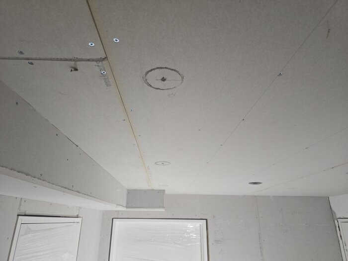 Gipstak förberett för målning med synliga skruvar och skarvar. Installationen är redo för målare att börja arbetet.