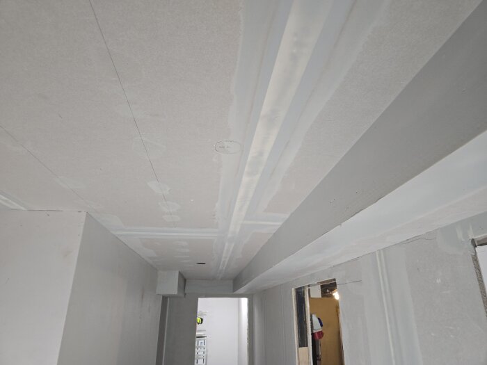 Innertak som nyligen spacklats, sett från sidan. Flera lager spackel syns ovanför dörröppningar i ett renoveringsprojekt.