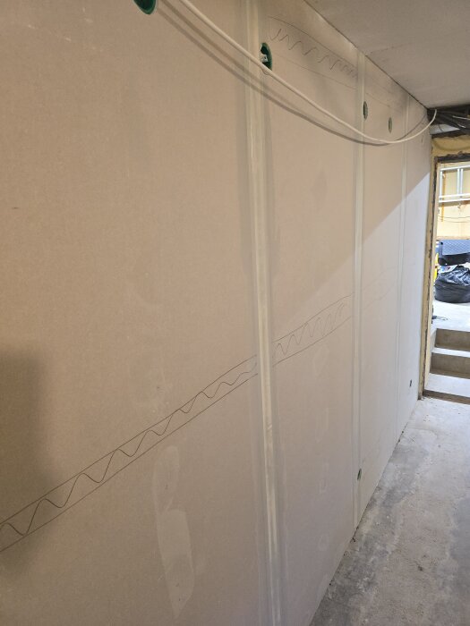 Nyuppsatta gipsskivor med skarvspackel på en vägg. Kablar syns längs väggen i ett renoveringsprojekt, ljusinsläpp från rummet bredvid.