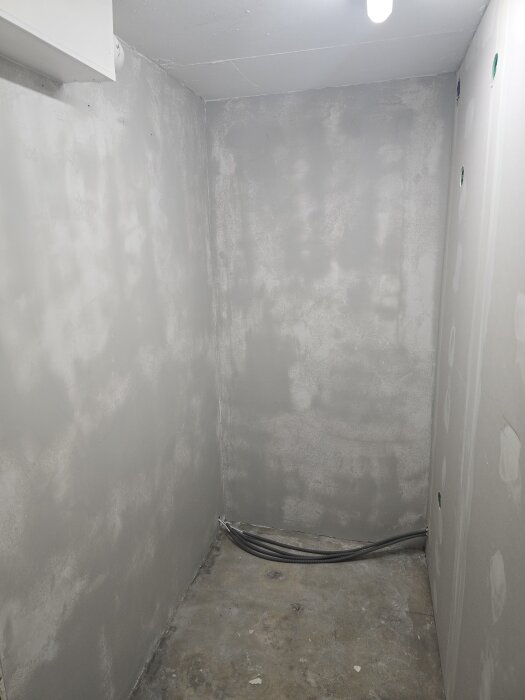 En gråputsad källarvägg med släta gipsskivor och några kablar längs golvet under förberedelse för målning.