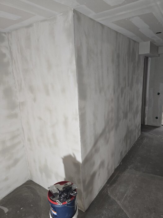 Nyligen bredspacklade väggar i ett källarrum med en hink full av verktyg framför. Förberett för målning nästa dag.