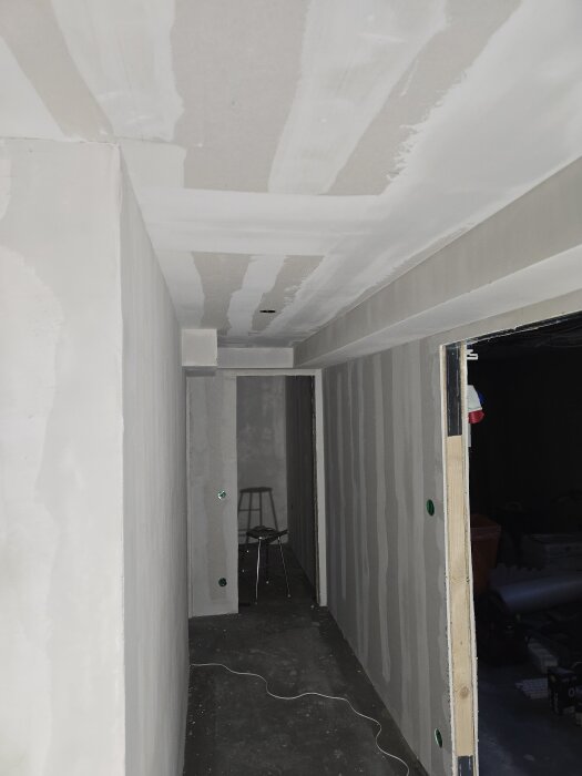 Källargång med nygipsskivade väggar och tak delvis spacklade, redo för målning. En pall syns längre in i korridoren.