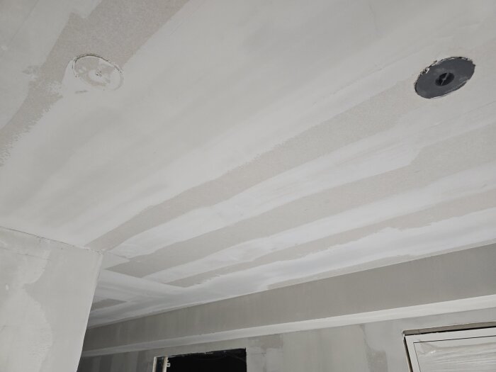Nymålat tak med installerade gipsskivor och två eluttag, redo för takspottar, innan målarna börjar sitt arbete.