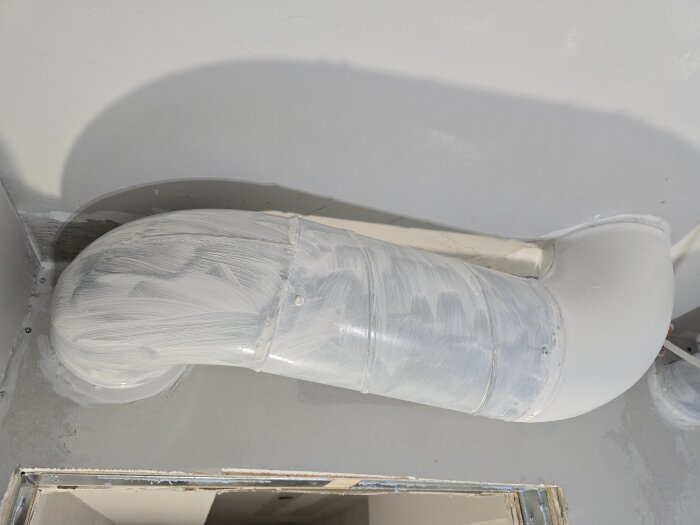 Ventilationsrör i ett utrymme, grundat med häftgrund som förberedelse inför målning.