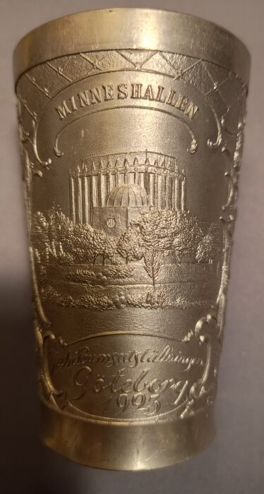Minnesbägare från Göteborgsutställningen 1923 med texten "MINNESHALLEN" och motiv av byggnad och träd, med graverad text "Jubileumsutställningen Göteborg 1923".