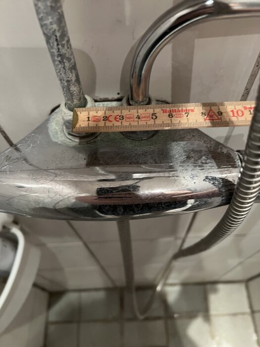 Duschblandare med mycket kalkavlagringar och ett måttband som mäter avståndet mellan rören.