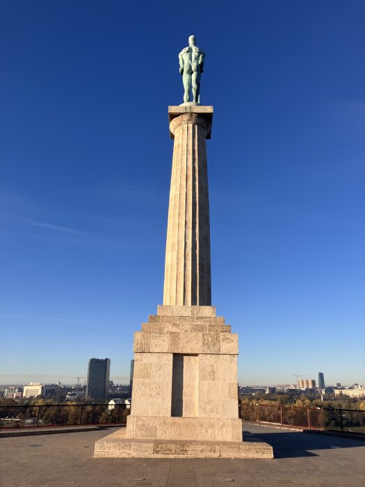 Staty av en man på en hög kolonn med stadshorisont i bakgrunden under en klarblå himmel.