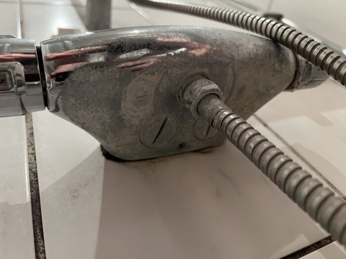 Närbild på en duschblandare med kalkavlagringar på ytan.