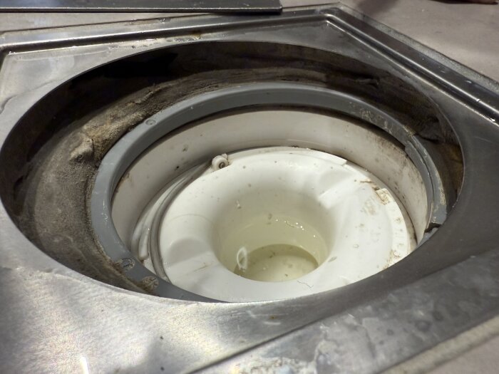 Golvbrunn med synlig grå tätring och spår av smuts inuti, potentiellt otät, i ett nyproducerat hus.