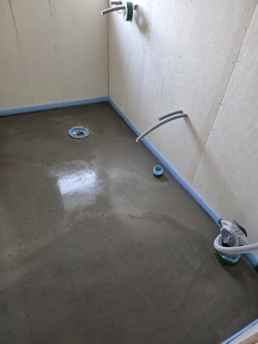 Nyflytspacklat badrumsgolv med rördragningar, förberett för installation av vägghängd toalett och golvvärme.
