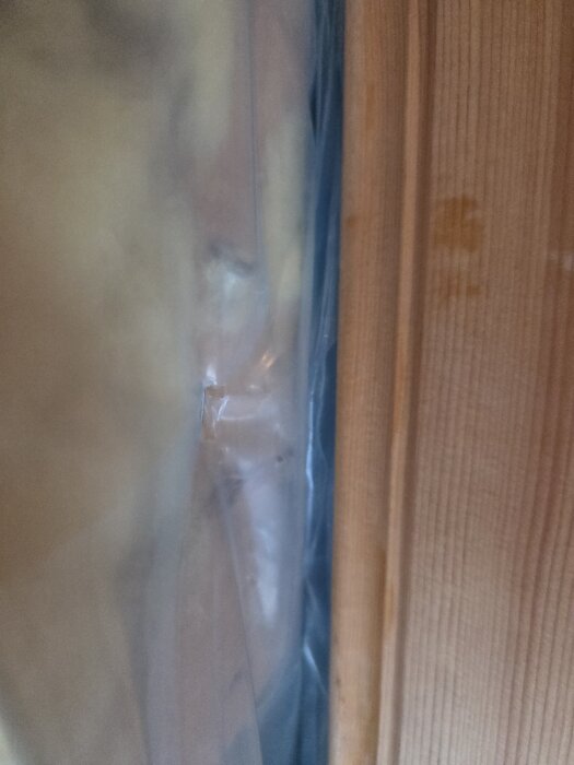 Fuktspärrsplast skadad vid skarv mellan tak och vägg, träpanel bredvid.