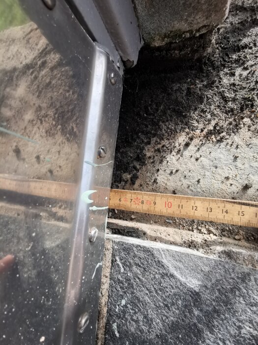 Tröskel över skiffertrappa med lös limning, metallkant och måttband som visar avstånd till stenen.