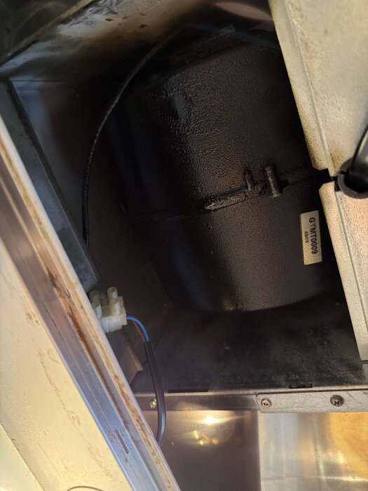 Inuti en köksfläkt från 2010 med en synlig fläktmotor och elektriska anslutningar, delvis täckt av fett.