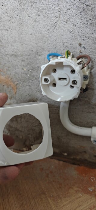 Vägguttag från Malmbergs under installation, visande kablage och skyddsplatta mot bakgrund av betongvägg och träyta.