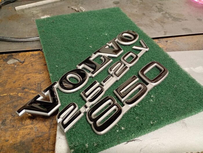 Klarlackade Volvo-emblem ligger på grön underlag, med tydliga detaljer utan penselspår.