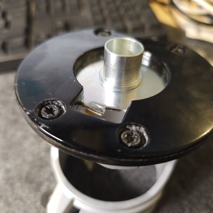 Monterad metallhylsa med fyra klackar i en svart bas med skruvar, ovanpå ett grått rör.