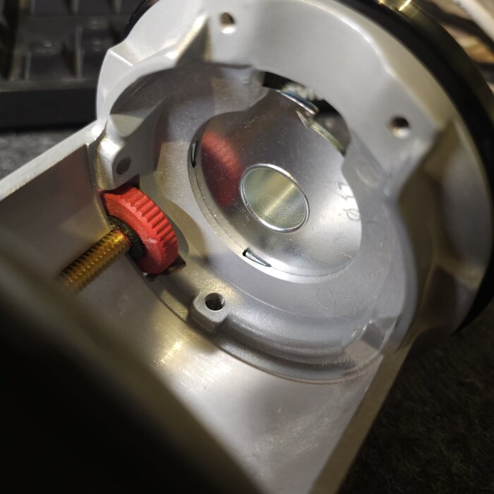 Närbild av en metallhylsa med fyra klackar som passar in i motsvarande gropar i en bas, med en synlig röd justeringskomponent och gängad skruv.