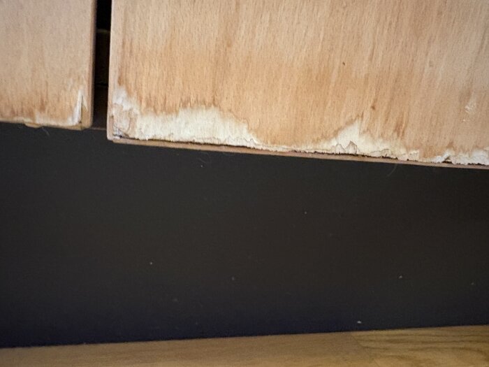 Slitna köksluckor i trä med skador längst ner, visa behovet av renovering eller byte.
