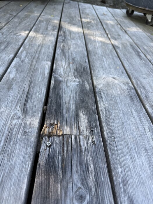 Slitna träplankor på en altan med skador och sprickor, fotograferade mitt på altanen ca 4,5 år efter bygge.